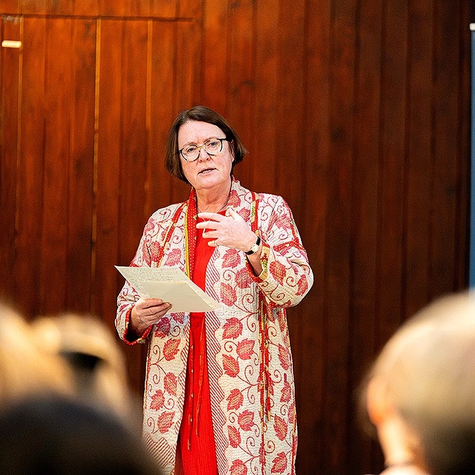  Wearing a long coat with a pattern of red leaves, one hand raised for emphasis, Professor Elwen Evans delivers a lecture on the theme of inspiring inclusion. 